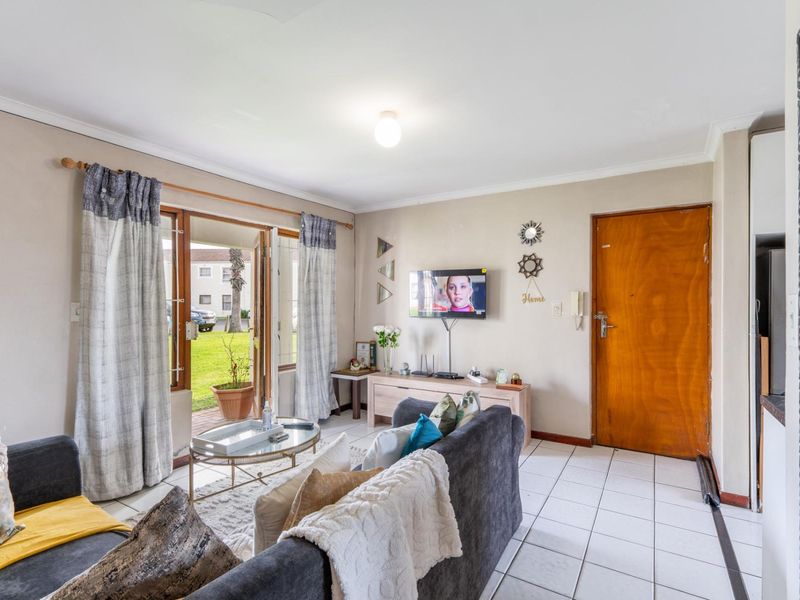 A bright living room featuring tiled flooring, a wooden entrance door, and a glass sliding door providing direct access to the outdoor garden area.