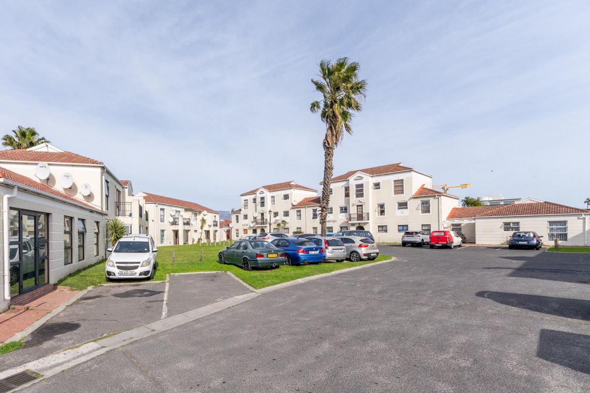 Exterior view of an apartment complex featuring a paved parking area, landscaped lawn, and multi-story residential buildings with tiled roofs.