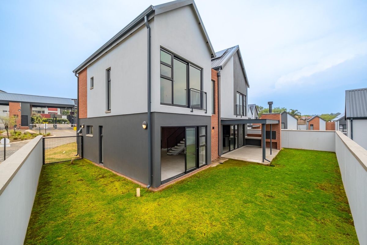 Rear view of a modern double-story home featuring a covered patio with a built-in braai, sliding glass doors, and a private garden.