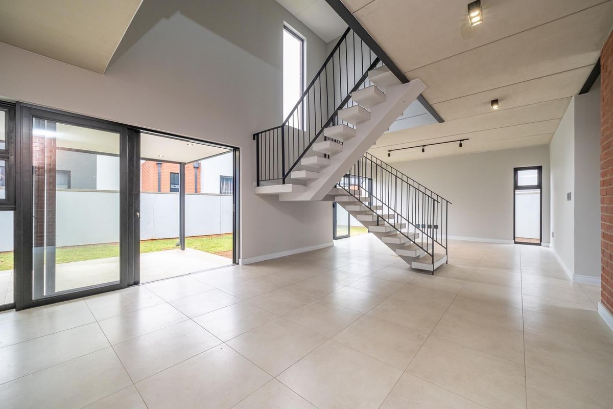 Spacious open-plan living area featuring a modern floating staircase, large sliding glass doors to the patio, and contemporary tiled flooring.