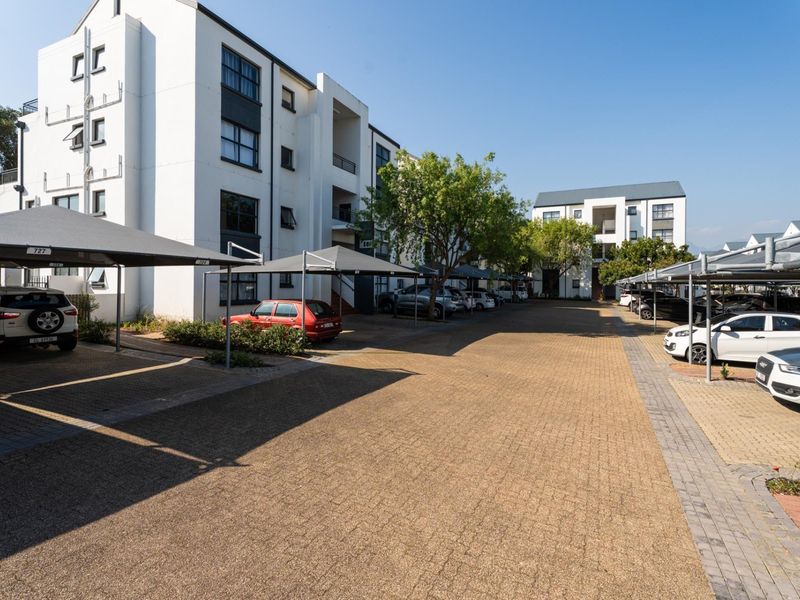 Exterior view of a modern apartment complex featuring paved parking areas with covered carports and well-maintained building facades.