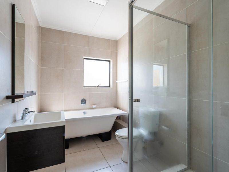 Modern bathroom featuring a freestanding bathtub, separate glass-enclosed shower, vanity unit, and neutral floor-to-ceiling tiling.