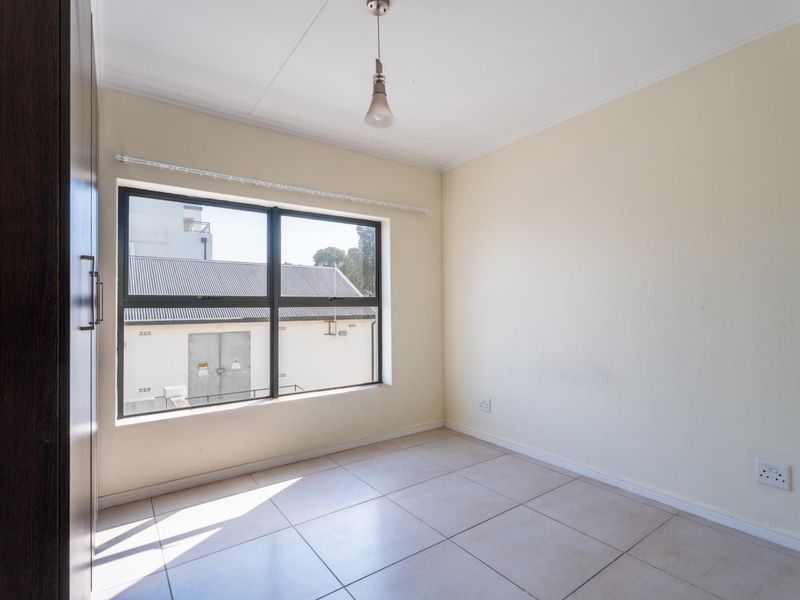 A bright, empty bedroom featuring neutral tiled flooring, a built-in wardrobe, and a large window providing natural light.