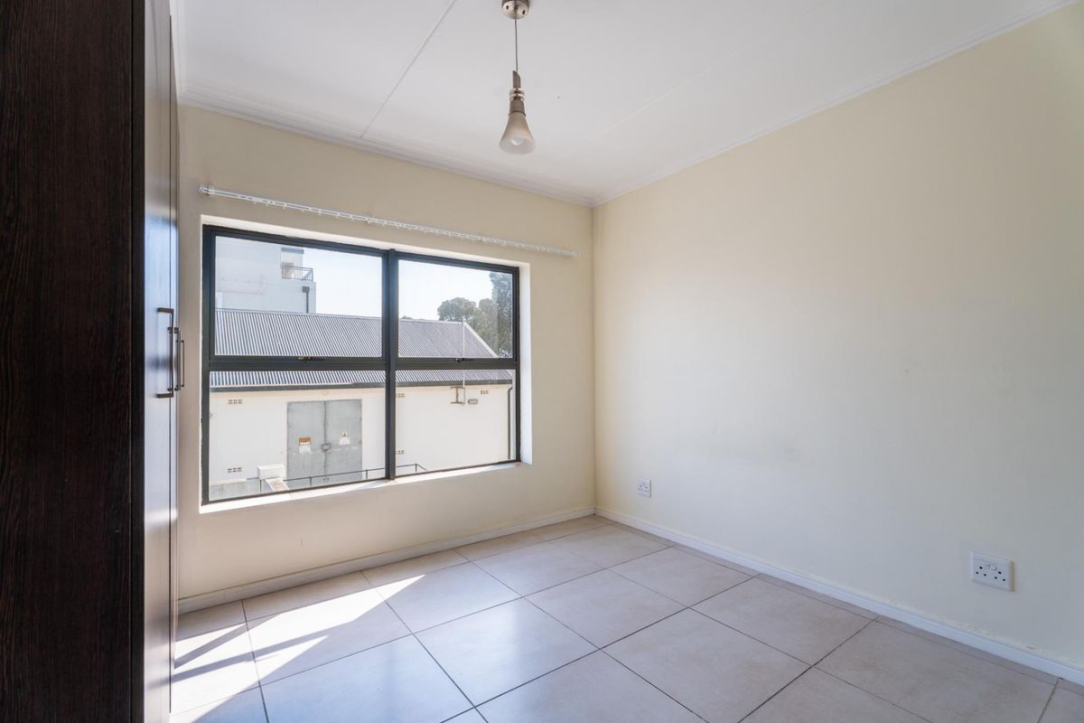 A bright, empty bedroom featuring neutral tiled flooring, a built-in wardrobe, and a large window providing natural light.
