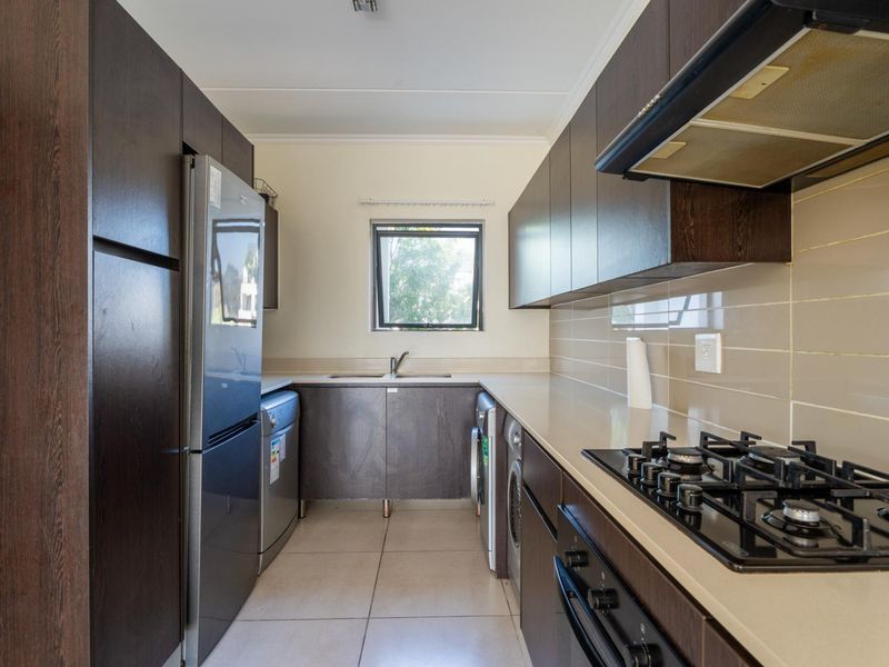 Modern galley-style kitchen featuring dark wood cabinetry, stone countertops, gas hob, integrated oven, extractor fan, and tiled flooring with a functional layout.
