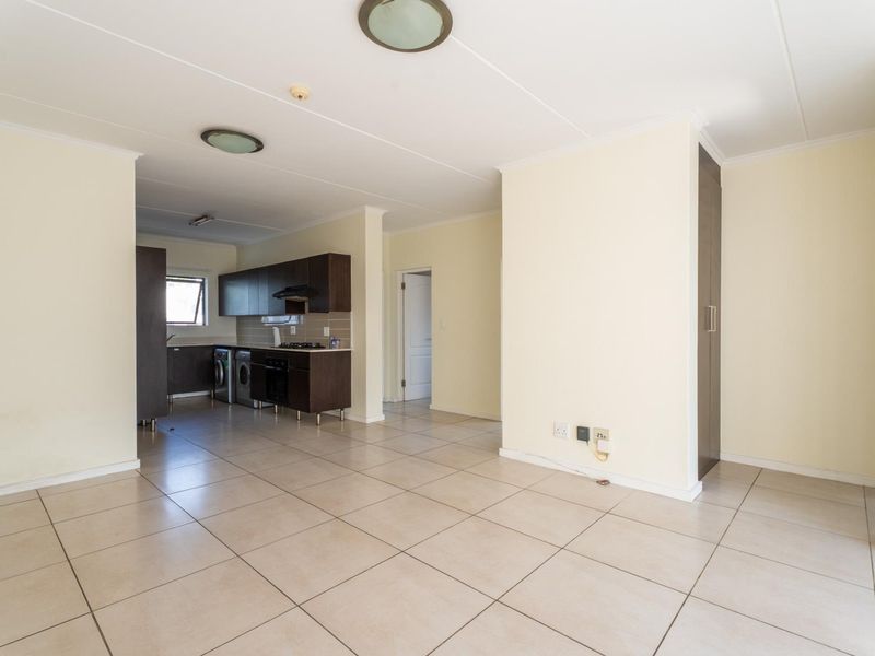 An open-plan living and kitchen area featuring neutral tiled flooring, dark wood-finish cabinetry, and built-in appliances, offering a clean and versatile living space.
