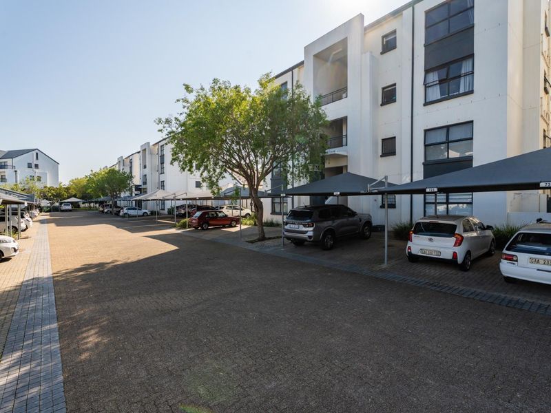 Exterior view of a modern apartment complex featuring paved driveway access and designated covered parking bays for residents.