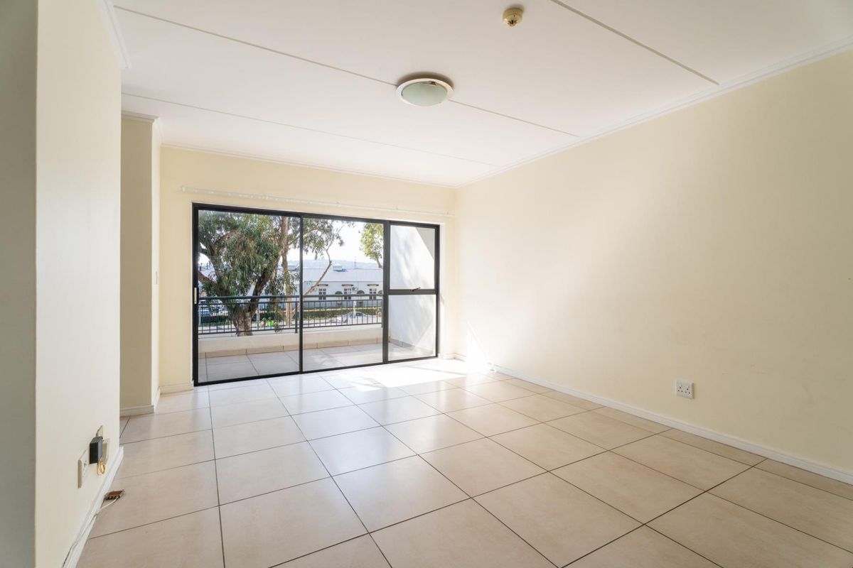 A bright, empty living room featuring neutral tiled flooring and a large sliding glass door that opens onto a balcony.