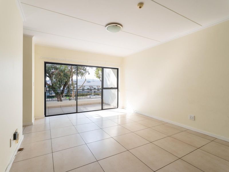 A bright, empty living room featuring neutral tiled flooring and a large sliding glass door that opens onto a balcony.