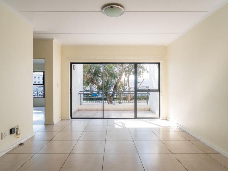 A bright, empty living room featuring neutral tiled flooring and a large sliding glass door that opens onto a private balcony.