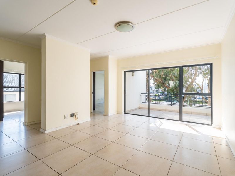 A bright, empty living room featuring neutral tiled flooring and a large sliding glass door providing access to an outdoor balcony.