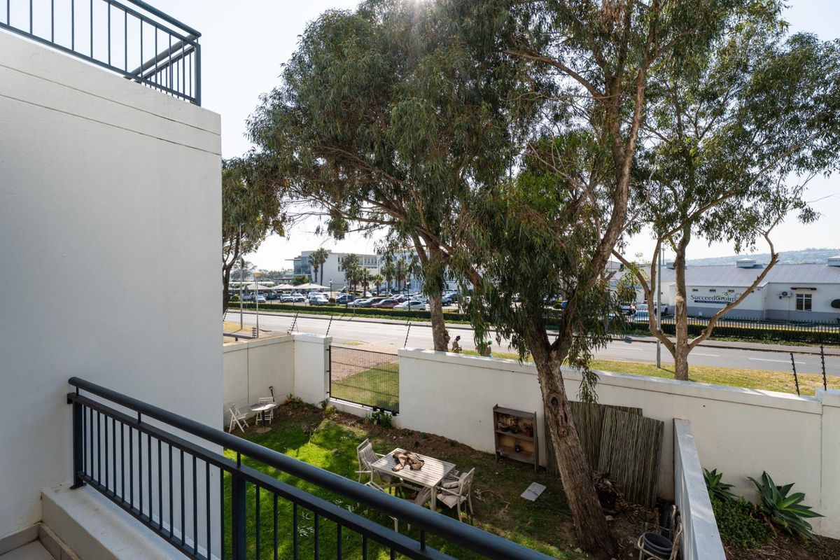 A view from an upper-level balcony overlooking a private rear garden area with boundary walls and electric fencing.