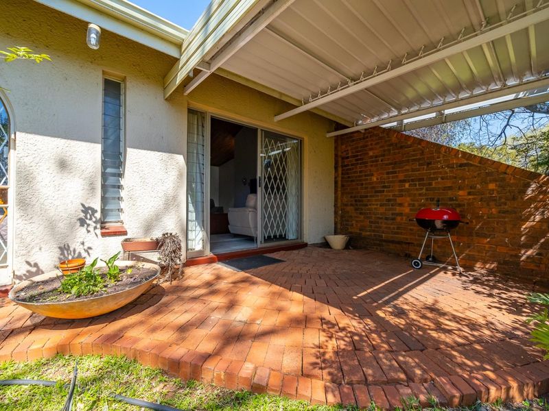 A covered brick-paved patio area featuring a brick feature wall, sliding door access to the interior, and louvered windows.