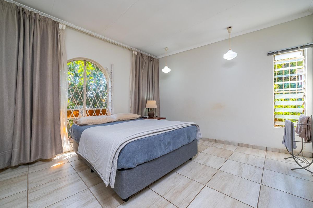 A bedroom featuring tiled flooring, an arched window with security gate, and pendant lighting, offering a functional space with potential for cosmetic updates.