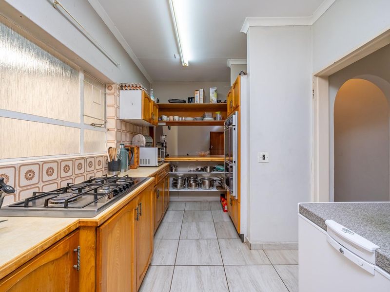 A functional kitchen featuring wooden cabinetry, a gas hob, built-in oven, and tiled finishes, offering potential for a modern renovation.