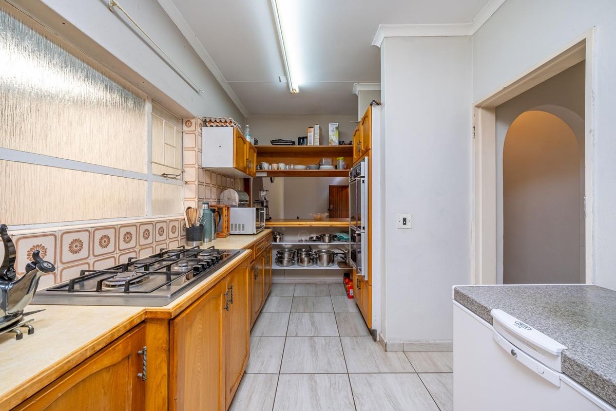 A functional kitchen featuring wooden cabinetry, a gas hob, built-in oven, and tiled finishes, offering potential for a modern renovation.