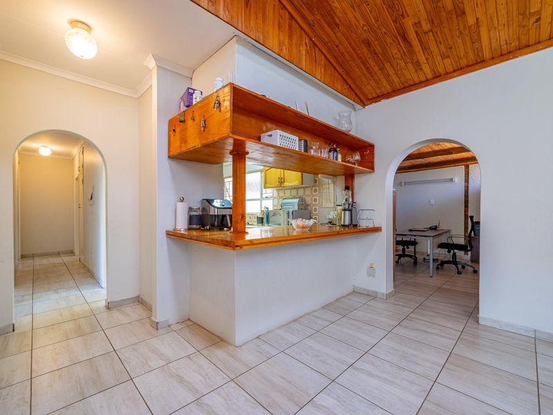 Open plan living area featuring a timber ceiling, tiled flooring, and a central breakfast bar with built-in shelving, connecting to adjacent rooms via archways.