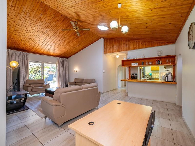 Open-plan living and dining area featuring a vaulted timber ceiling, tiled floors, and a breakfast bar connecting to the kitchen.