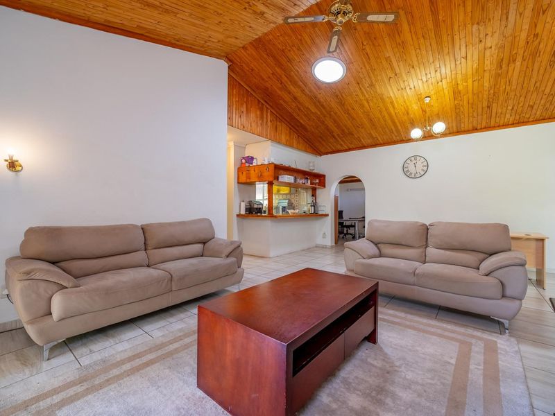 Open-plan living area featuring a vaulted timber ceiling, tiled flooring, and a convenient pass-through window connecting to the kitchen space.
