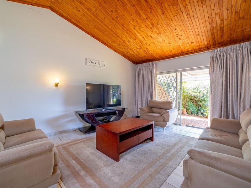 Spacious living room featuring a vaulted timber ceiling, tiled flooring, and direct access to the rear patio through sliding glass doors.