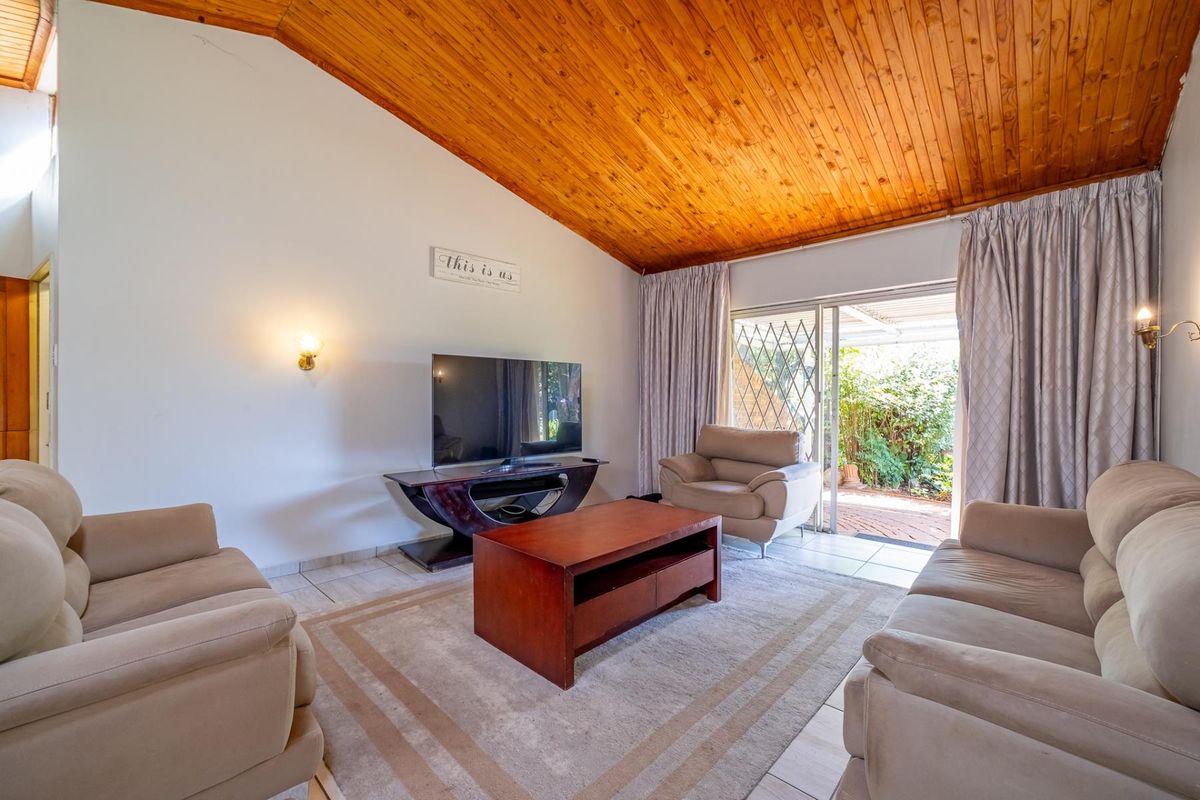 Spacious living room featuring a vaulted timber ceiling, tiled flooring, and direct access to the rear patio through sliding glass doors.