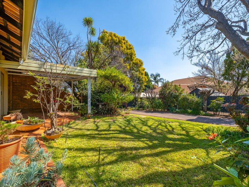 A well-maintained rear garden featuring a covered patio area with brick paving, established trees, and a lush lawn.