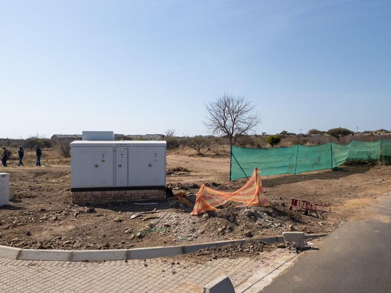 A vacant commercial land plot featuring an installed electrical transformer box, paved curbing, and temporary construction fencing.
