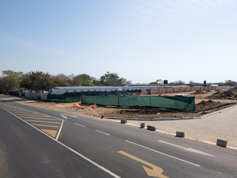 A view of a commercial vacant land plot featuring paved road access, boundary walls, and ongoing site preparation work.