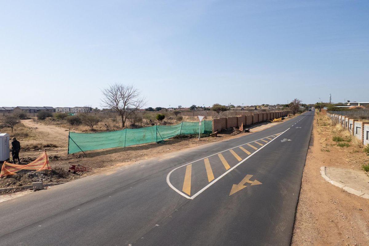 A view of the paved road and street frontage adjacent to the vacant commercial land, featuring existing boundary walling and road markings.