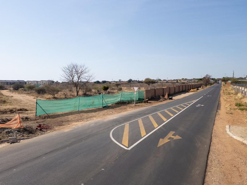 A view of the paved road and street frontage adjacent to the vacant commercial land, featuring existing boundary walling and road markings.