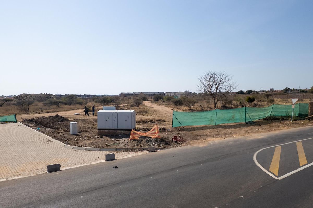 A view of a vacant commercial land plot featuring an electrical transformer box, paved entrance, and perimeter fencing adjacent to an asphalt road.