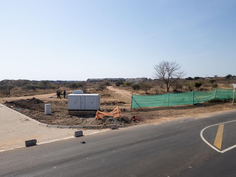 A view of a vacant commercial land plot featuring an electrical transformer box, paved entrance, and perimeter fencing adjacent to an asphalt road.