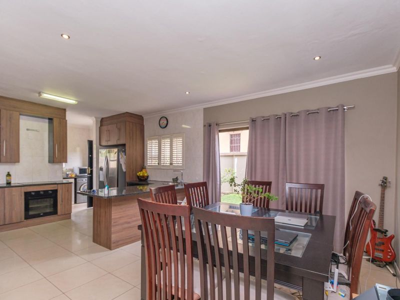 Open-plan kitchen and dining area featuring modern wood-finish cabinetry, granite countertops, built-in appliances, and tiled flooring with direct access to the outdoor space.