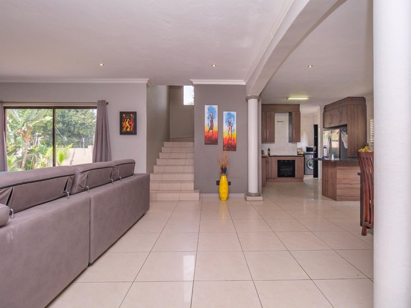 Spacious open-plan living area featuring tiled floors, a modern kitchen with built-in cabinetry, and a staircase leading to the upper level.