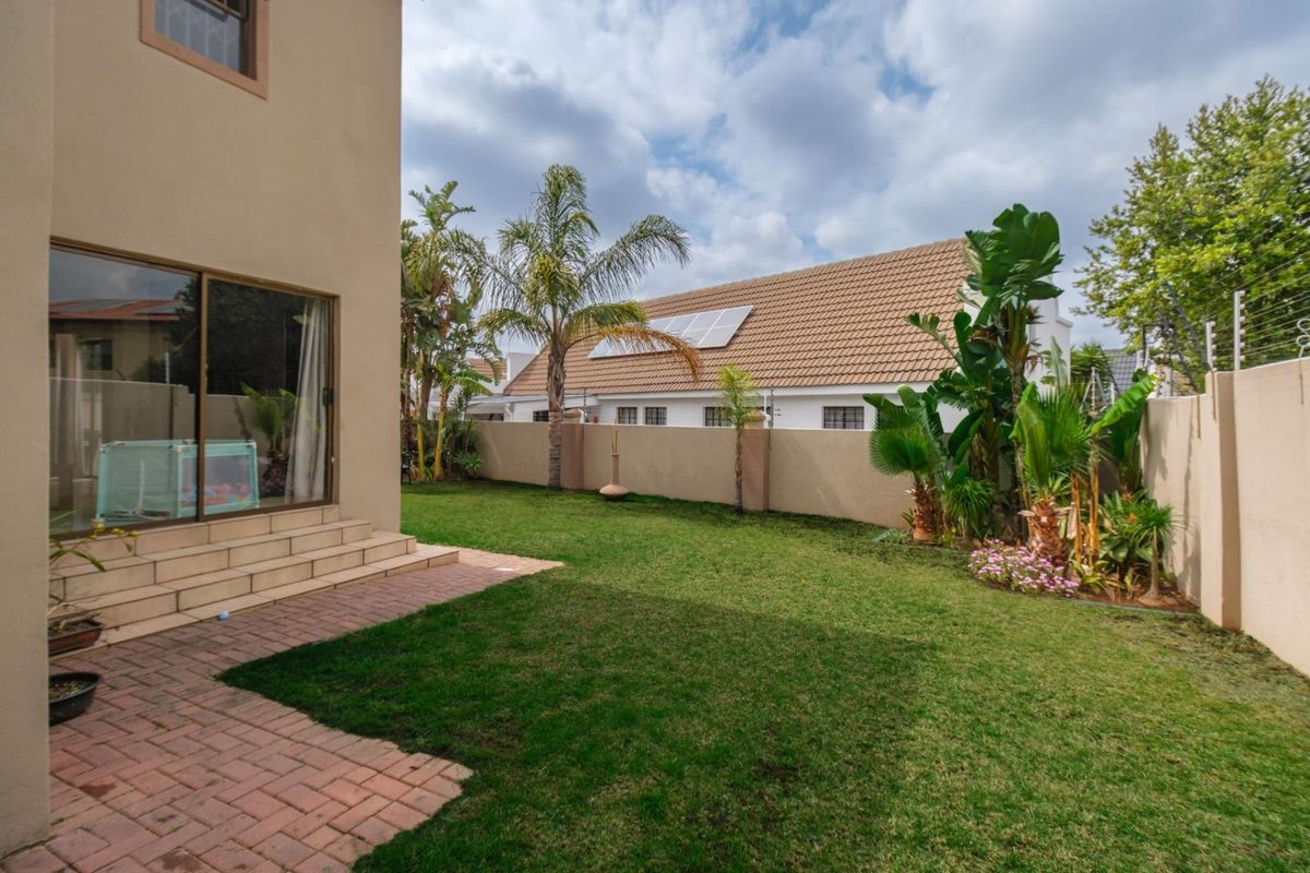 A private rear garden featuring a paved patio area, well-maintained lawn, perimeter boundary walls with electric fencing, and direct access to the home.