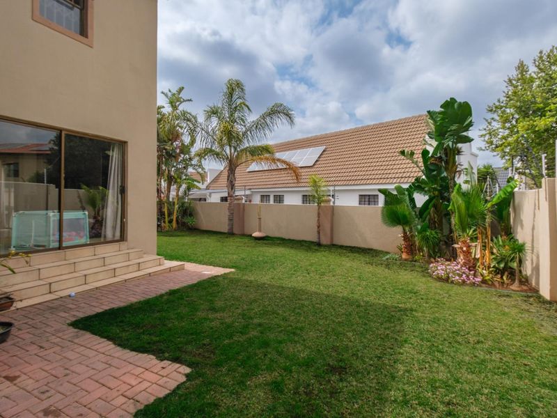 A private rear garden featuring a paved patio area, well-maintained lawn, perimeter boundary walls with electric fencing, and direct access to the home.