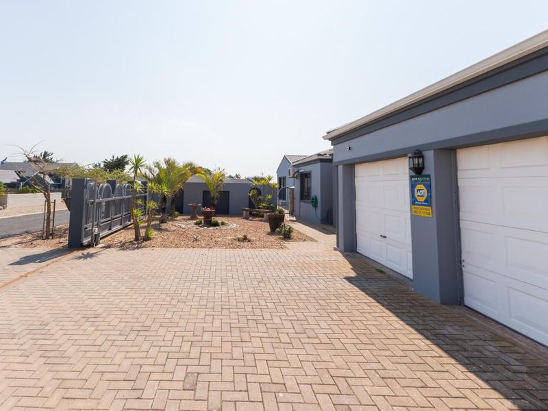 Front exterior view featuring a paved driveway, double garage, and landscaped garden area with security gate and perimeter wall.