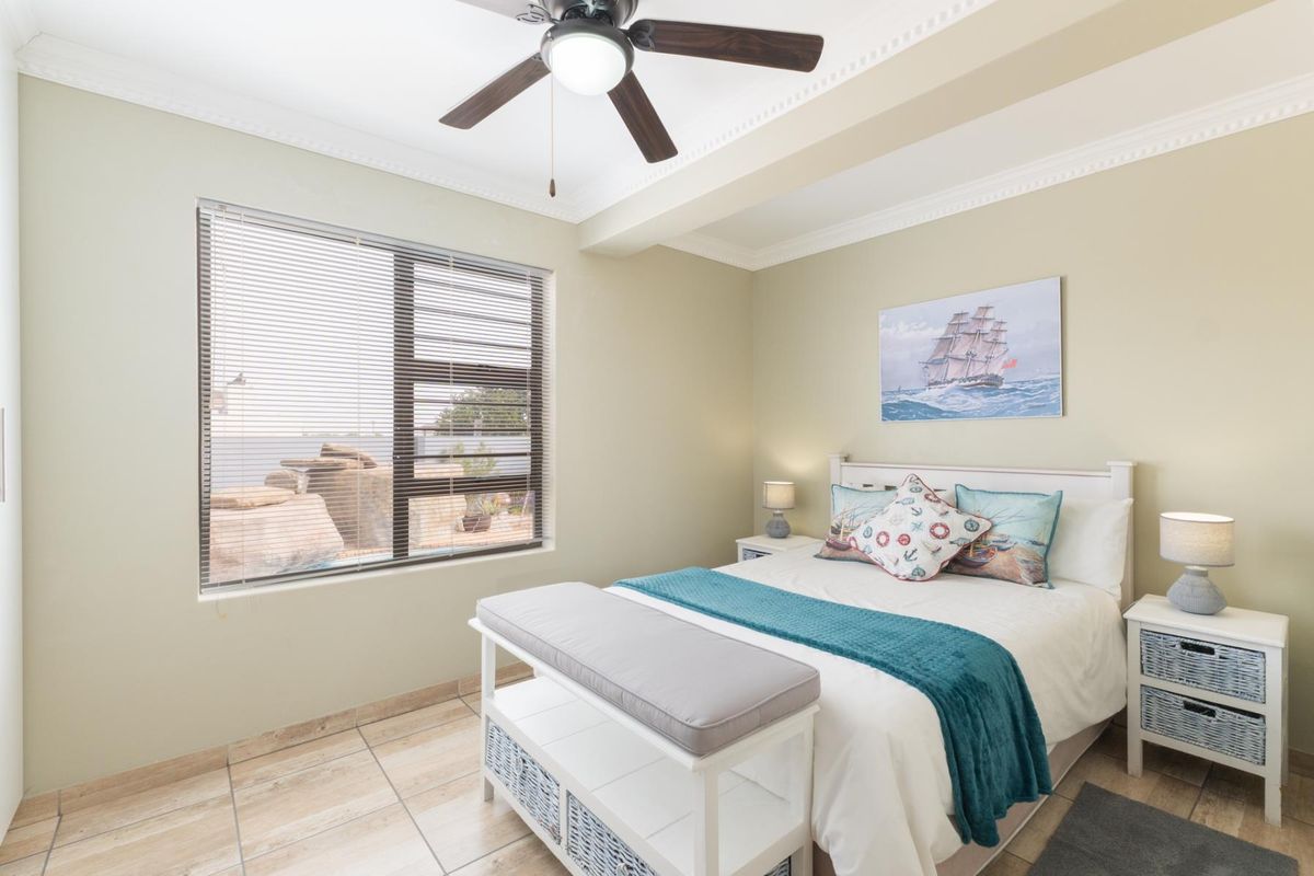 A well-maintained bedroom featuring tiled flooring, a ceiling fan, and large aluminium-framed windows providing natural light.