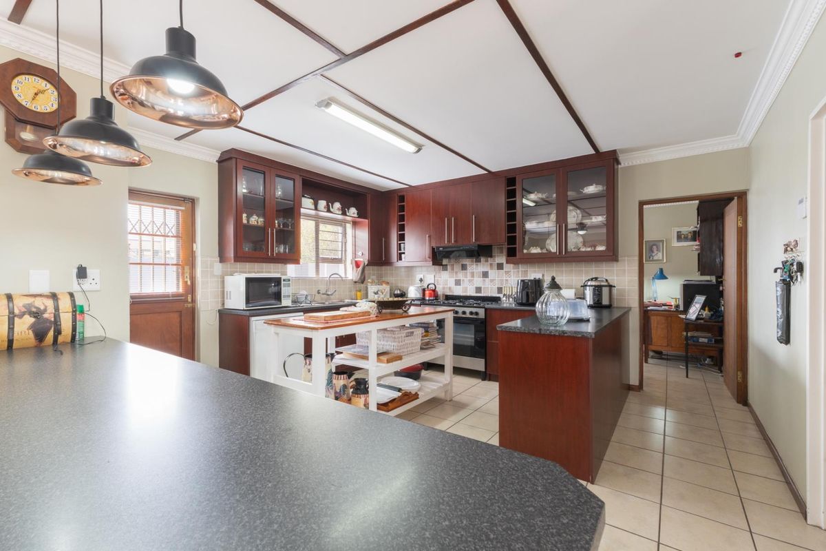 A functional kitchen featuring dark wood cabinetry, granite countertops, tiled backsplash, and a central island, with direct access to an adjacent room.