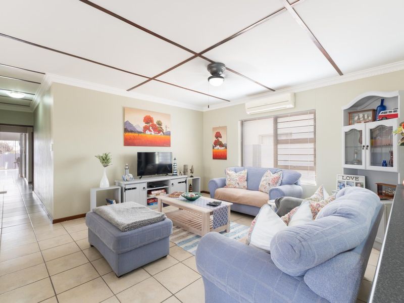 A comfortable living room featuring tiled flooring, a ceiling fan, and a wall-mounted split-system air conditioner, providing a functional and well-maintained living space.