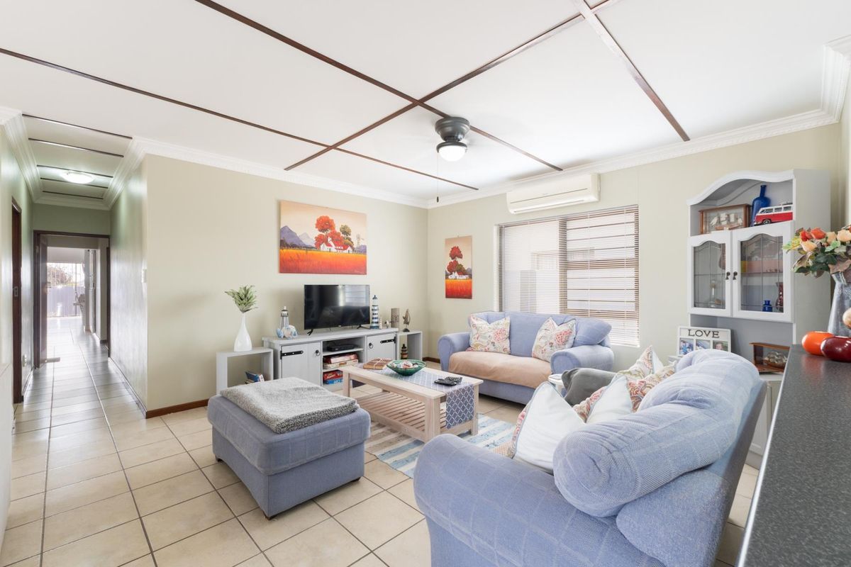 A comfortable living room featuring tiled flooring, a ceiling fan, and a wall-mounted split-system air conditioner, providing a functional and well-maintained living space.