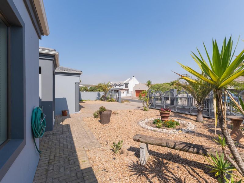 A view of the front exterior area featuring a paved walkway, gravel landscaping, and secure metal perimeter fencing.