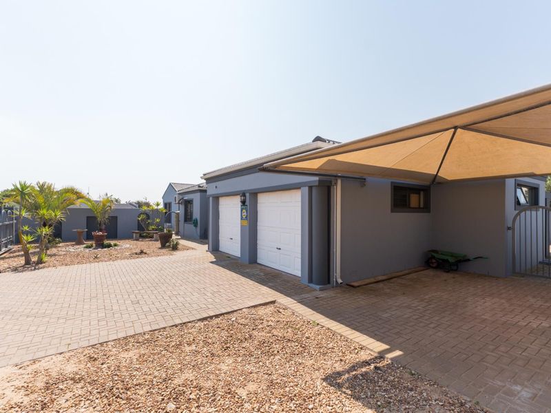 Front exterior view of the property featuring a double garage, paved driveway, and a shade sail carport structure.