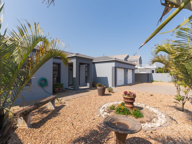 Front view of a modern house featuring a double garage, paved driveway, and a low-maintenance gravel garden with established palm trees.