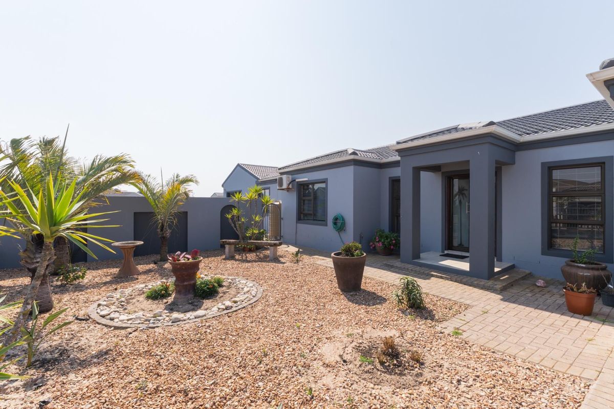 A well-maintained rear exterior view featuring a paved walkway, gravel garden area, and modern grey facade with a tiled roof.
