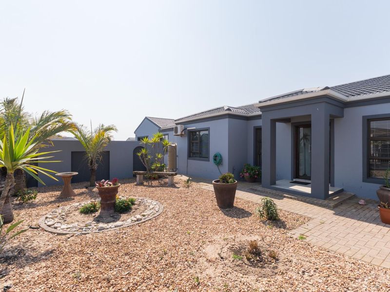 A well-maintained rear exterior view featuring a paved walkway, gravel garden area, and modern grey facade with a tiled roof.