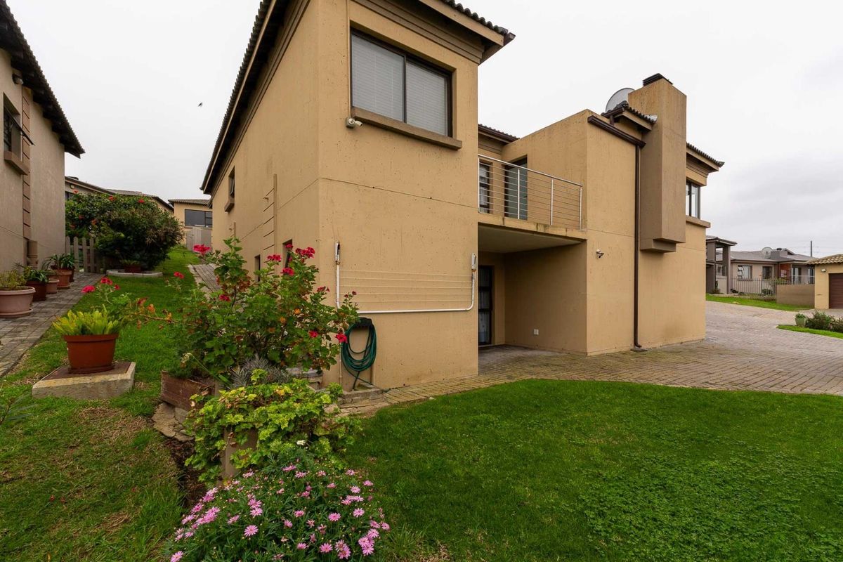 Rear view of a two-story residential property featuring a balcony, chimney, paved driveway, and a well-maintained lawn area.