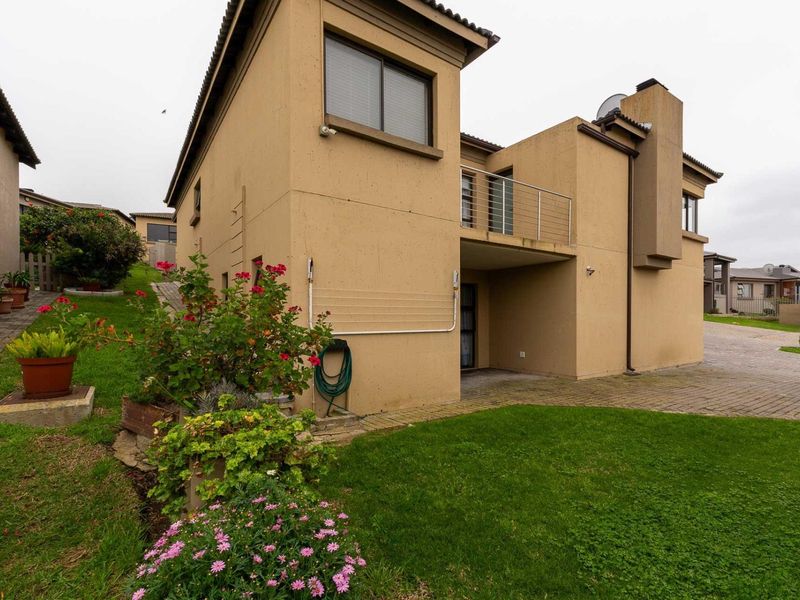 Rear view of a two-story residential property featuring a balcony, chimney, paved driveway, and a well-maintained lawn area.
