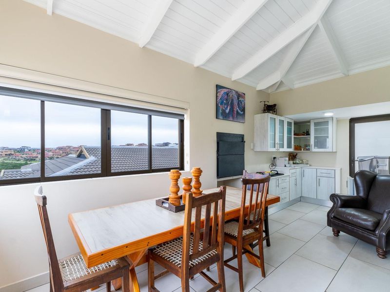 Open-plan living and kitchen area featuring a vaulted ceiling with exposed beams, tiled flooring, and a built-in fireplace with scenic exterior views.