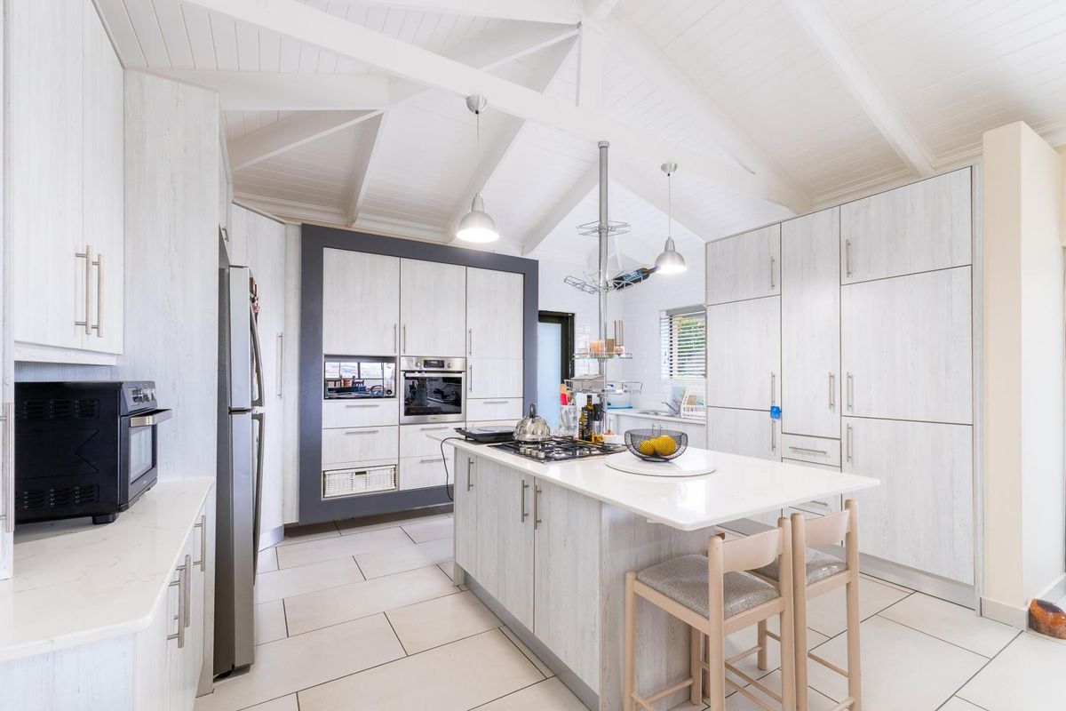 Modern kitchen featuring a central island with gas hob, built-in appliances, light wood-grain cabinetry, and a high vaulted ceiling with exposed beams.